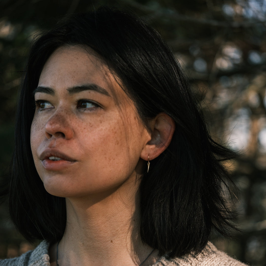 model wearing gold catbrier thorn earrings, white pines in background