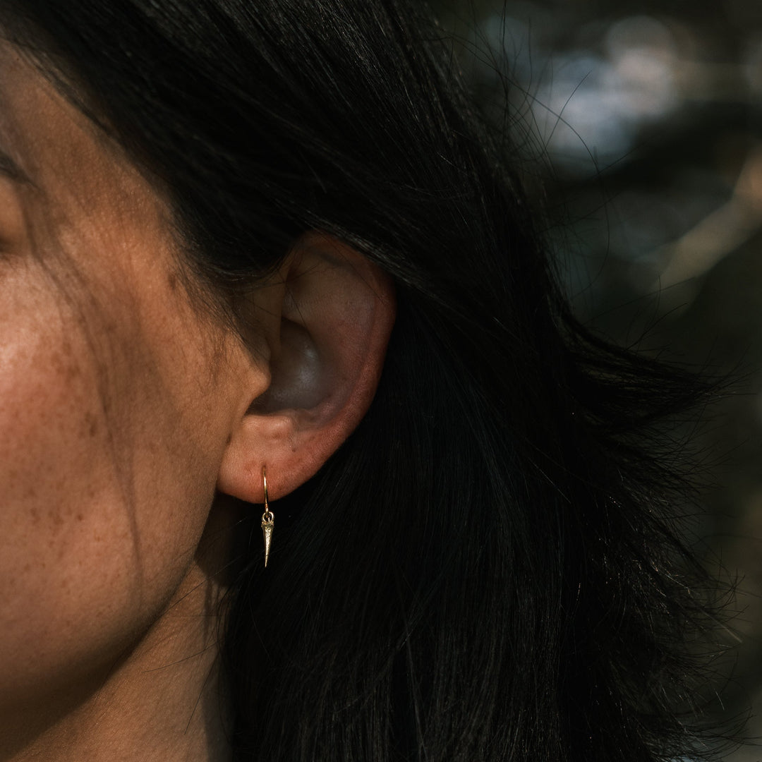model wearing gold catbrier thorn earring standing in front of pine trees