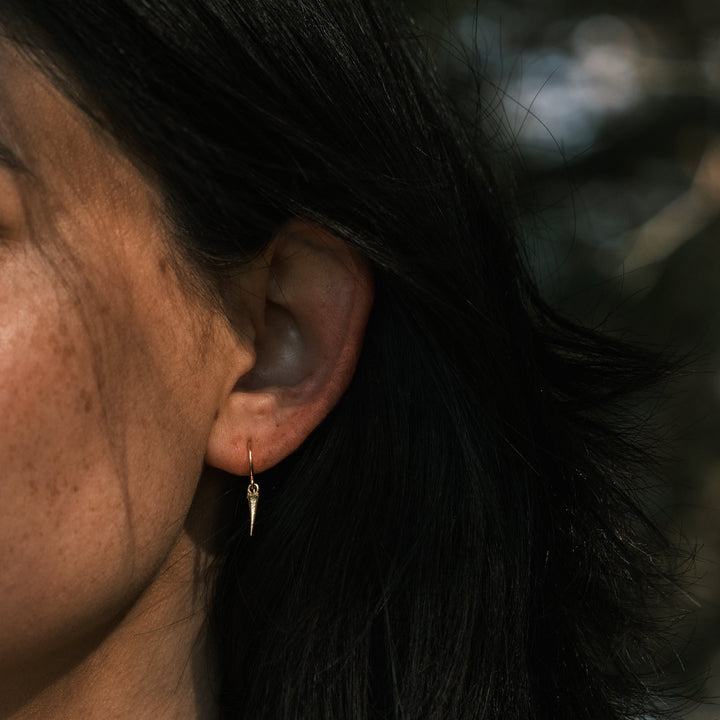 model wearing gold catbrier thorn earring standing in front of pine trees