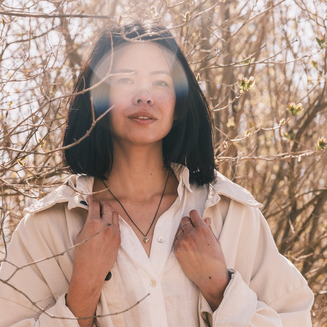 ocean pebble necklace worn with white shirt and white jacket, lilacs in background