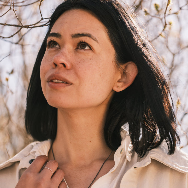 model wearing tiny vertebra stud earrings, white shirt and white jacket, lilacs in the background