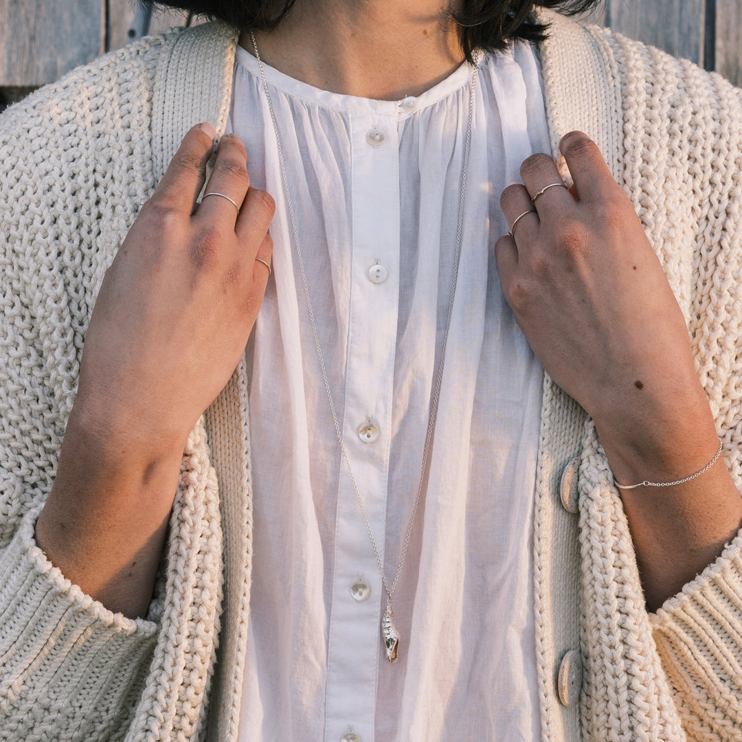 swallowtail chrysalis necklace worn with white sweater and white shirt, shingles in background