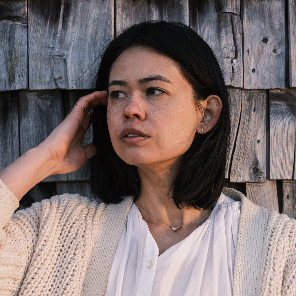 model wearing gold catbrier thorn studs, white shirt, and white sweater with shingles in the background