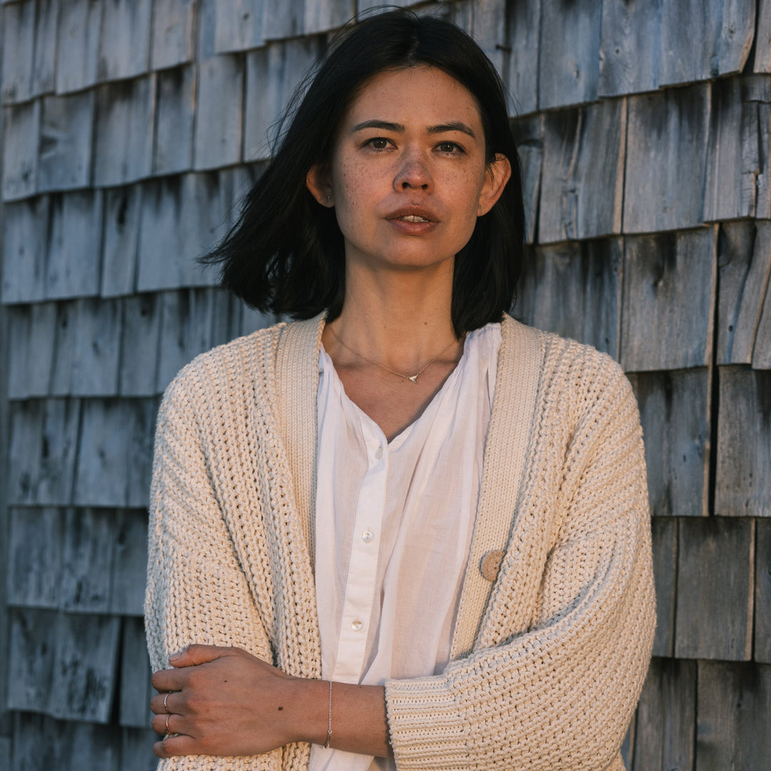gold wild rose thorn necklace worn with white shirt and white sweater, weathered shingles in background