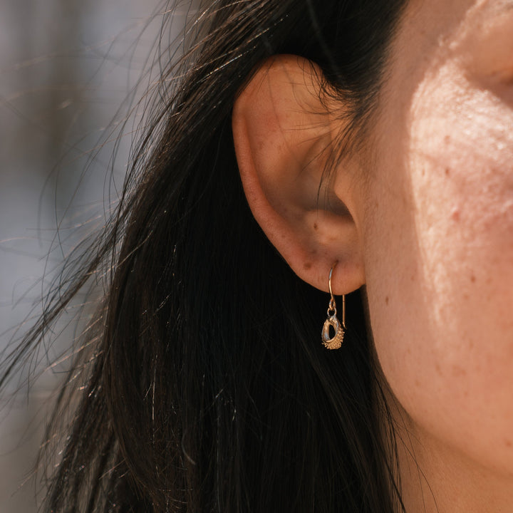 close up of model wearing gold calendula seed earrings