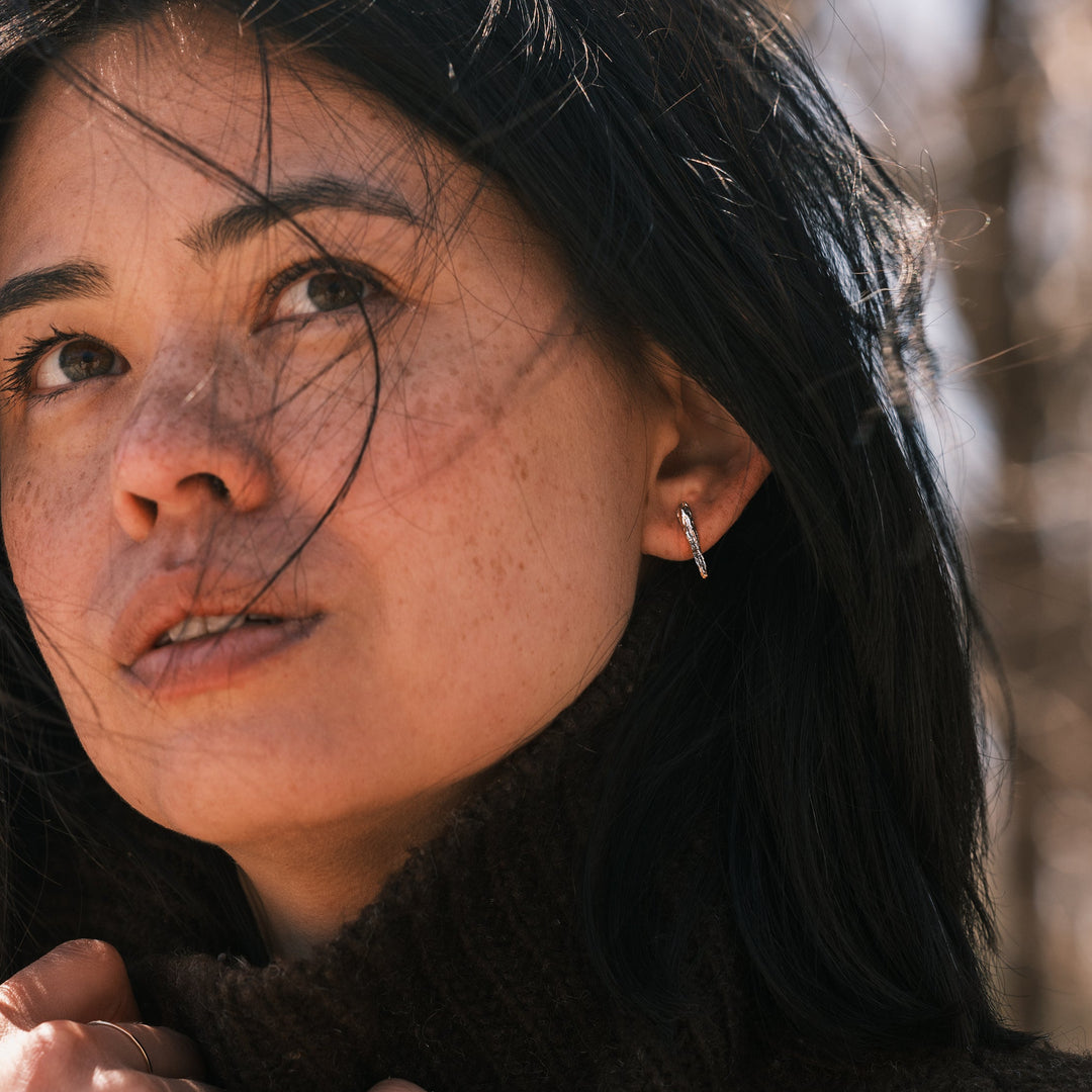 model wearing silver phyllite stud earrings and brown sweater on a windy day
