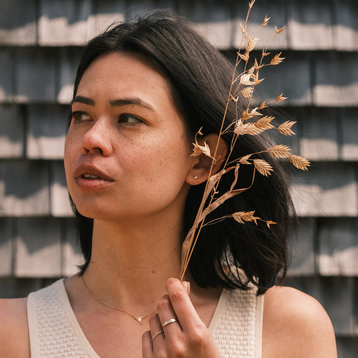 model wearing blackberry thorn studs and white lace dress, weathered shingles in background