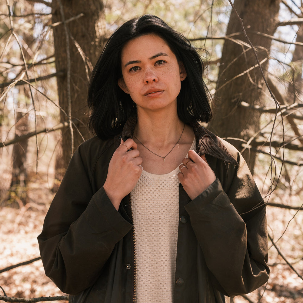 gold catbrier thorn necklace worn with lace dress and waxed canvas jacket, pine trees in background