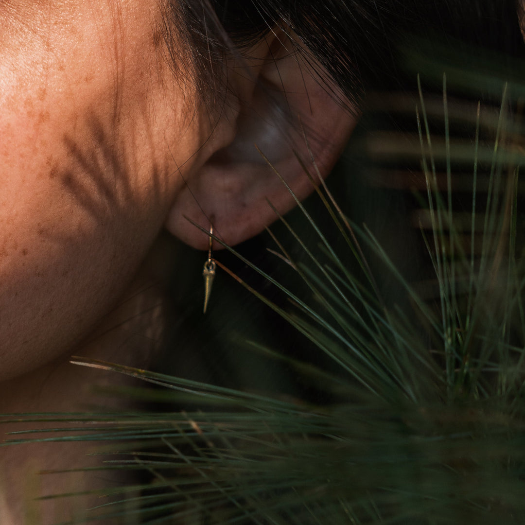 close up of catbrier thorn earring with model's ear and pine needles