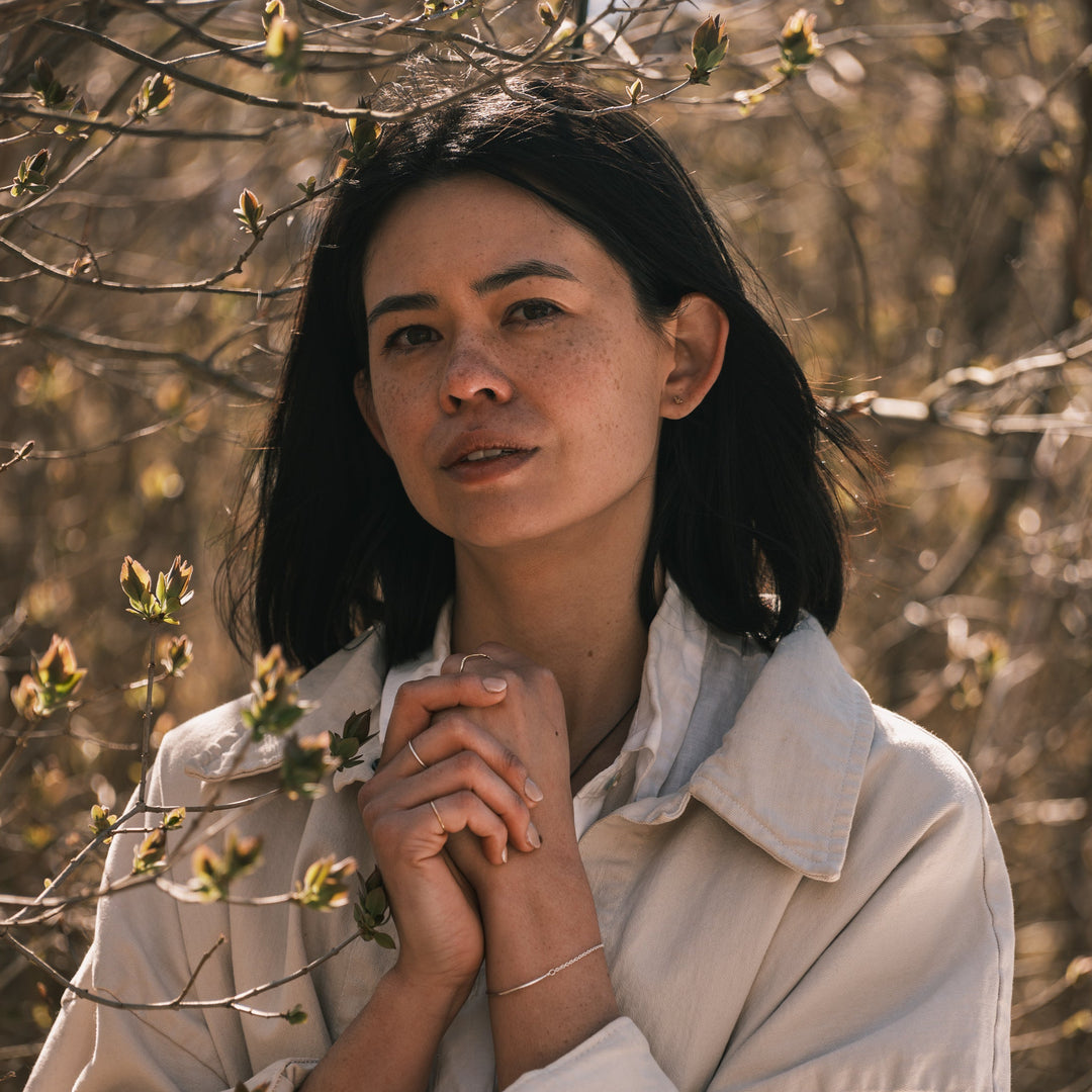 model wearing tiny vertebra stud earrings surrounded by budding lilacs