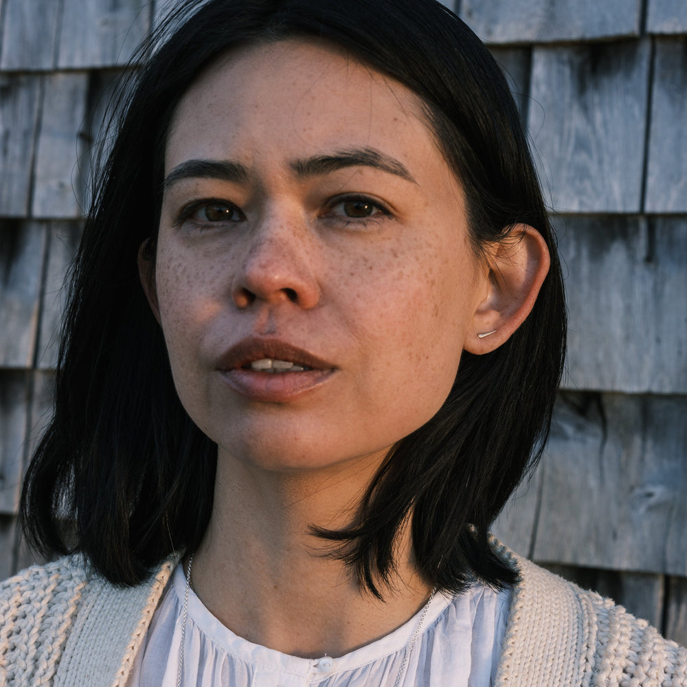 model wearing catbrier thorn studs and white shirt and sweater, weathered shingles in the background
