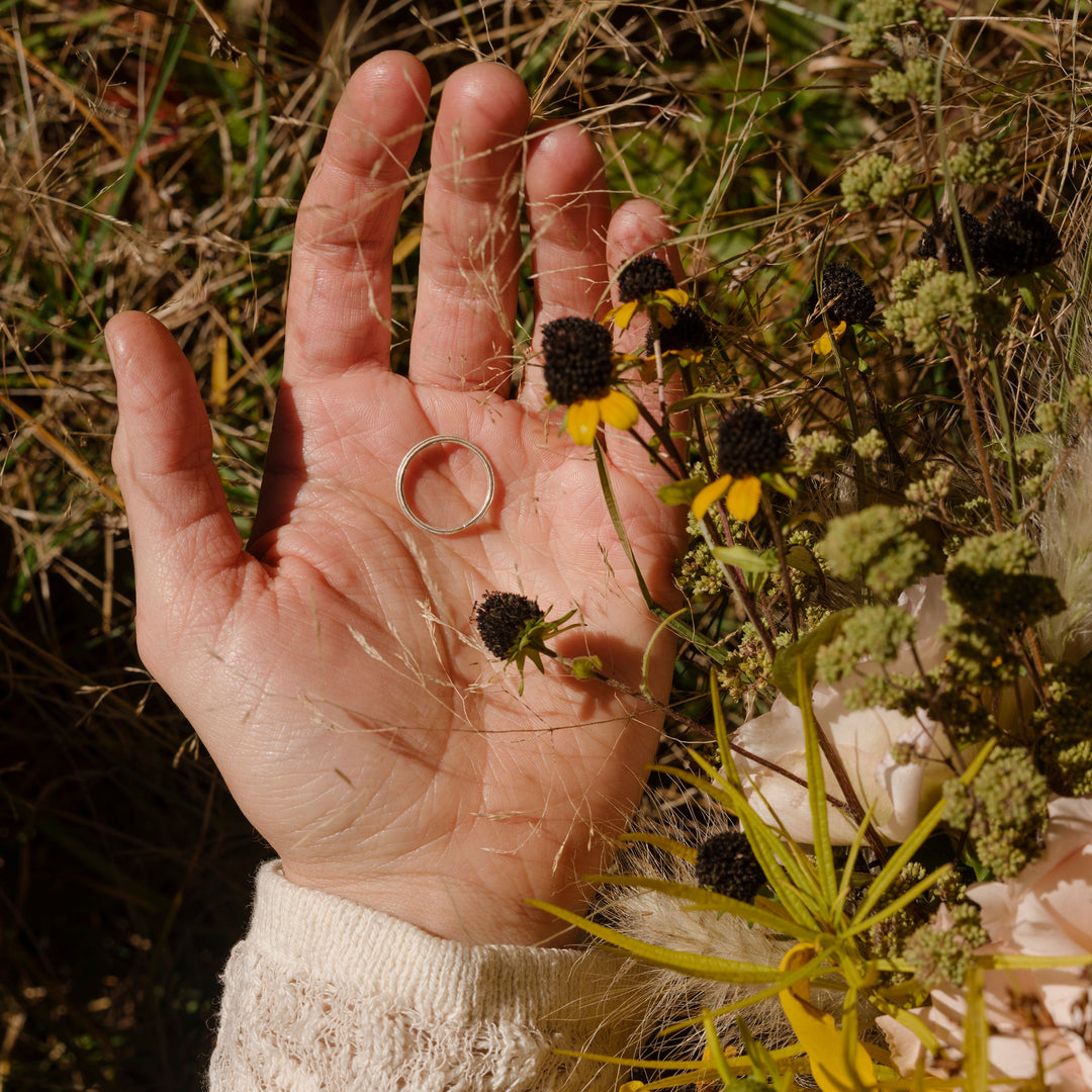 Hand holding a small black-eyed Susan flower with a blurred natural background